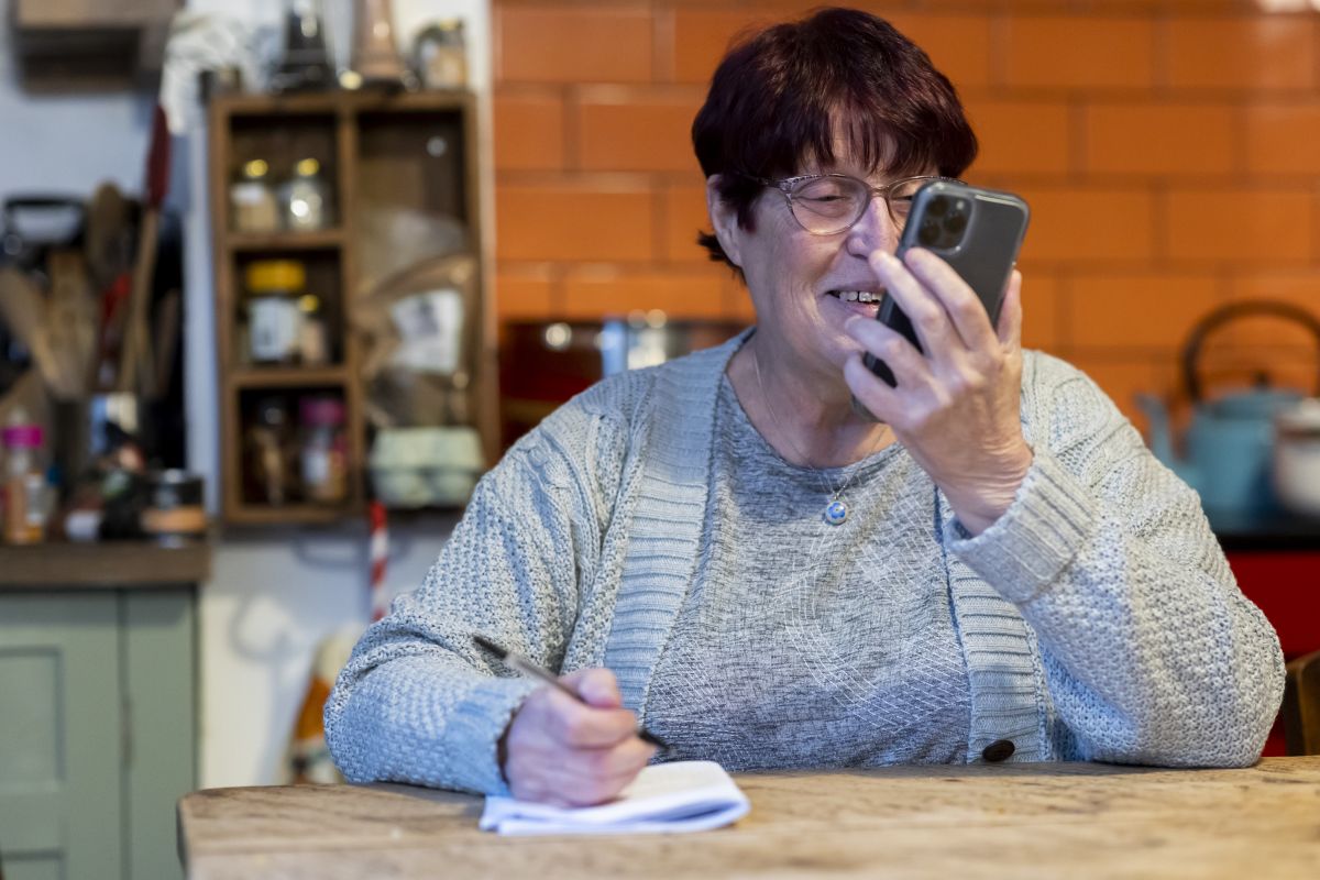 Photo of a woman sat at a table on the phone with a pen and notebook to hand