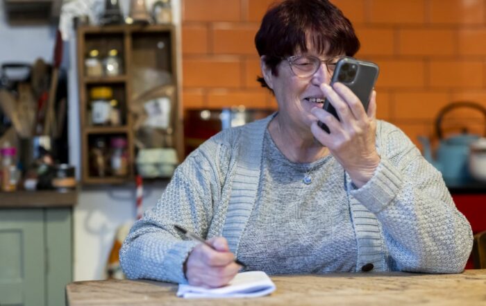 Photo of a woman sat at a table on the phone with a pen and notebook to hand