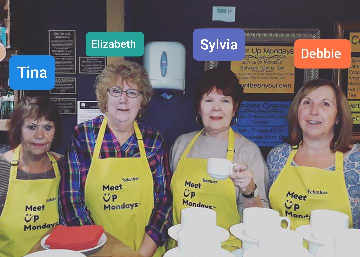 photo of the team at the Fisher Theatre Bungay's MeetUpMondays MUM's Broadcasting Service. Four ladies in yellow MeetUpMondays aprons standing behind cafe counter