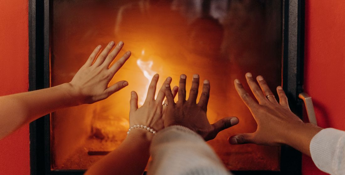 photo of people's hands stretched out to warm them in front of a fireplace